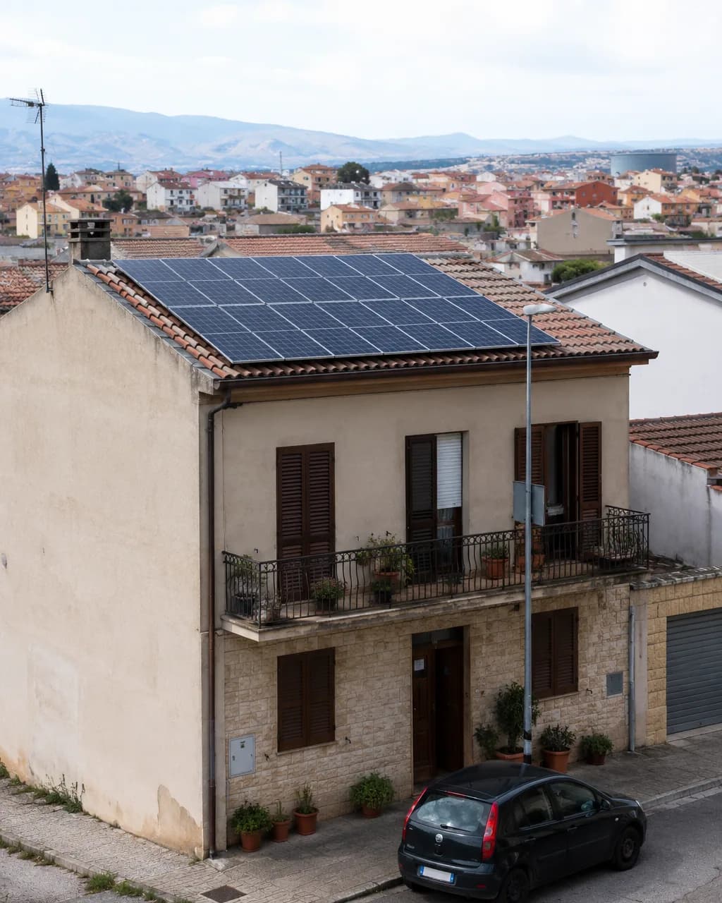 Casa di un paese sardo con pannelli fotovoltaici sul tetto, con il centro abitato e le colline sullo sfondo